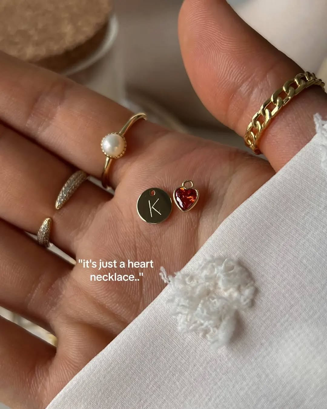 Hand wearing multiple rings with a focus on a small heart-shaped pendant.